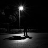 Silhouette of a person standing under a bright streetlight on a dark road at night