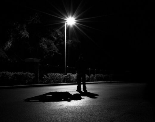 Silhouette of a person standing under a bright streetlight on a dark road at night