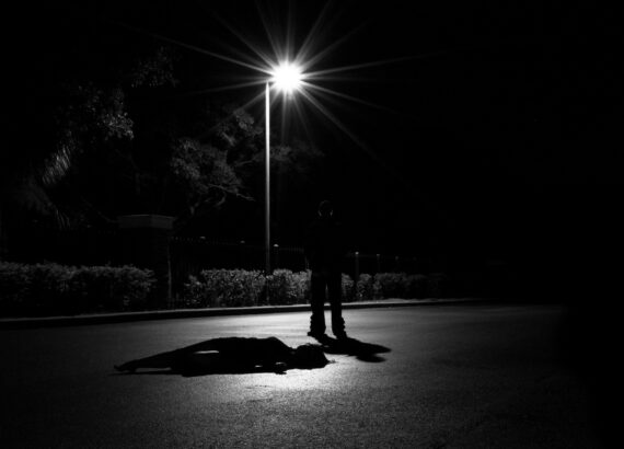 Silhouette of a person standing under a bright streetlight on a dark road at night